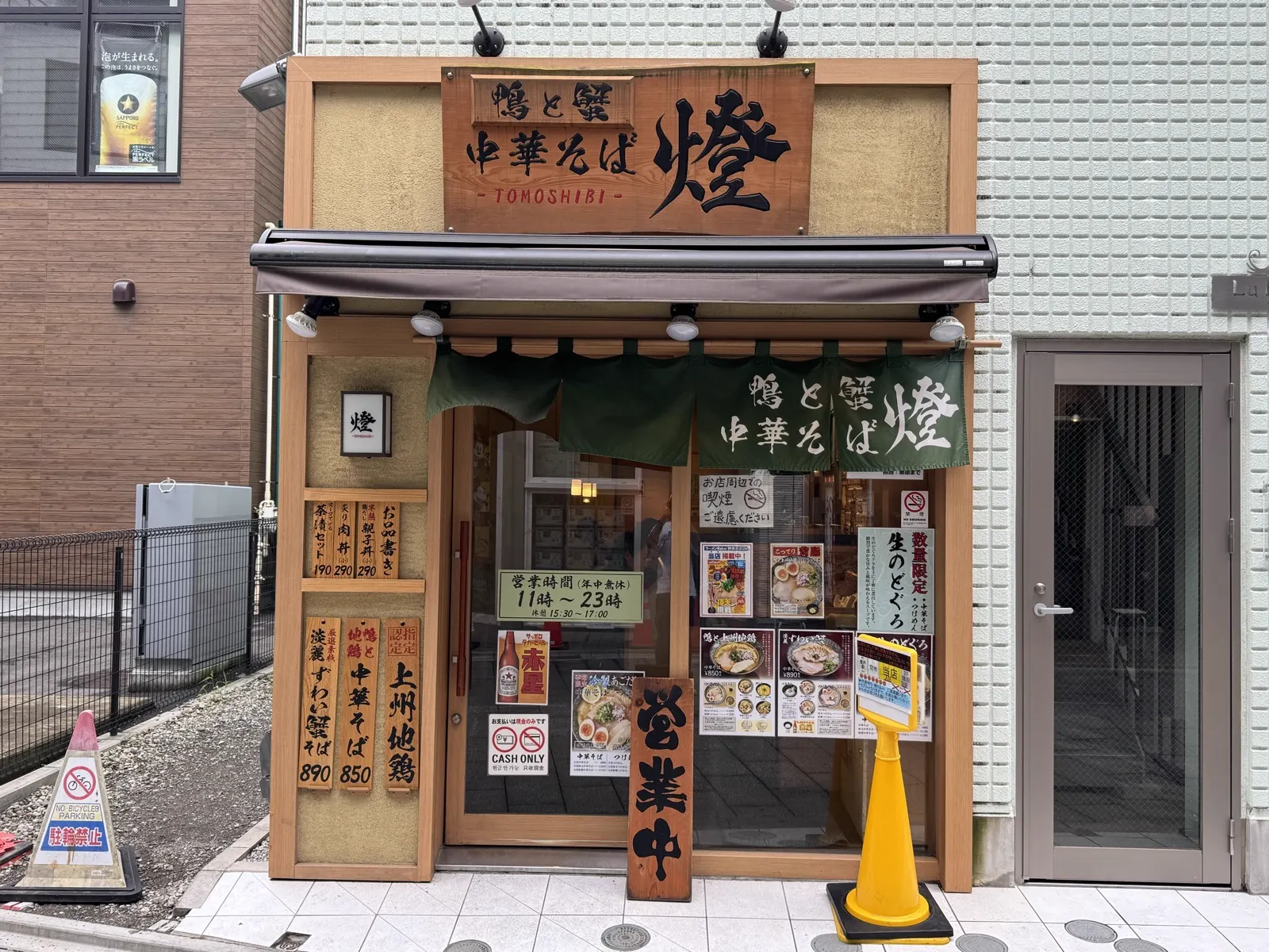 中華そば 燈(TOMOSHIBI)の外観 — 看板に CASH ONLY サインが貼られた職人系ラーメン店の典型例。鴨と蟹の限定中華そば、ガラス越しに券売機が見える