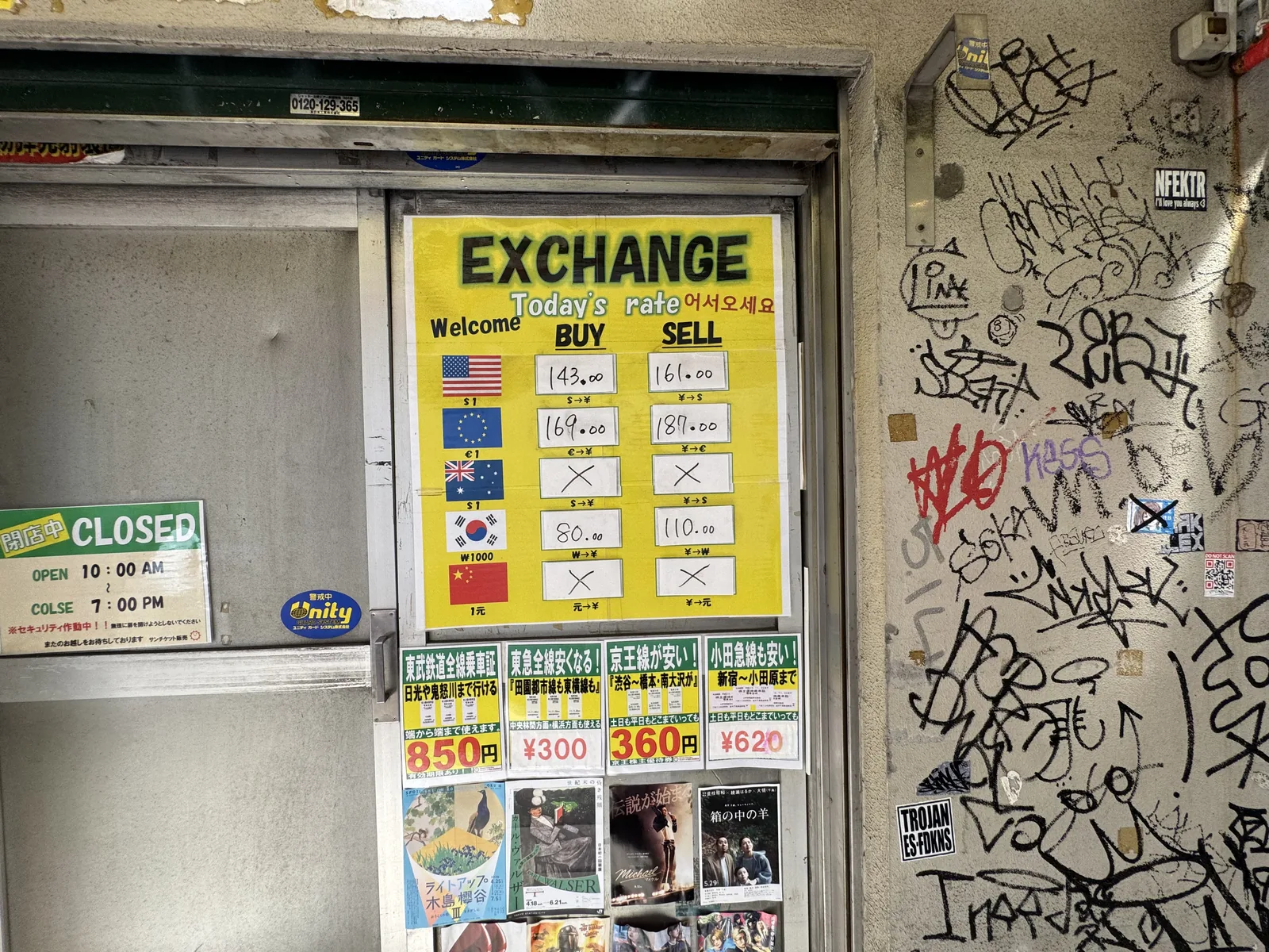 A bright yellow EXCHANGE rate board outside a small Shibuya money changer, listing BUY/SELL rates for major currencies — always check these against the live mid-market rate