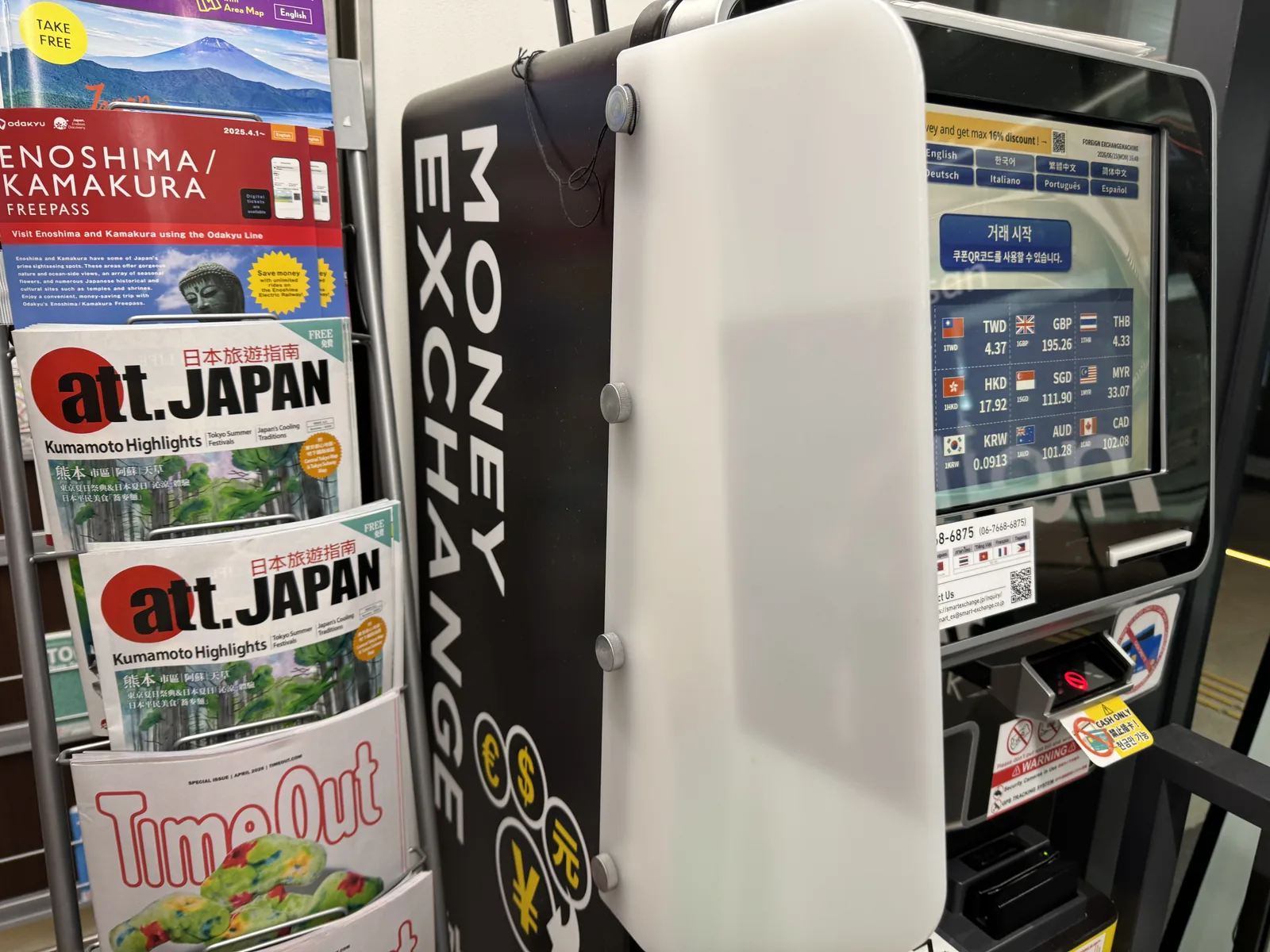 A row of automated currency-exchange machines lined up inside a Tokyo retail venue, each showing live rate displays