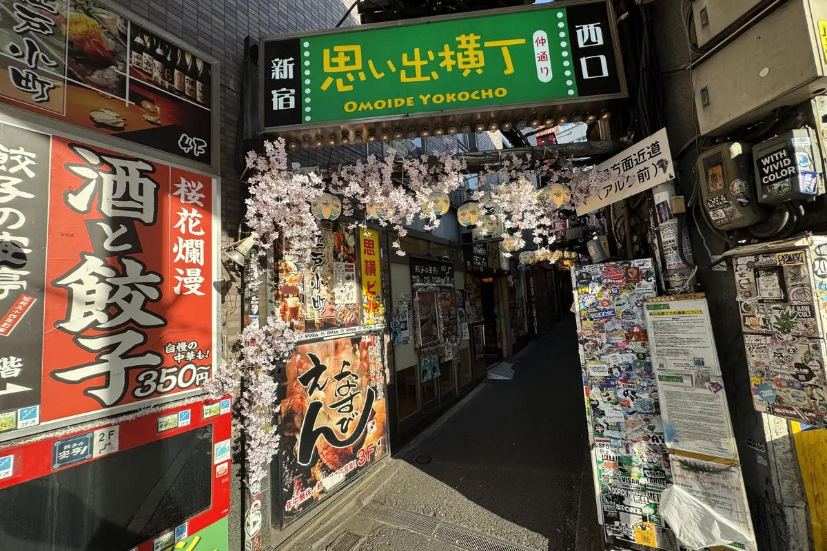 新宿西口の思い出横丁 入口ゲート — 「OMOIDE YOKOCHO」の看板と桜、現金カルチャー保護区
