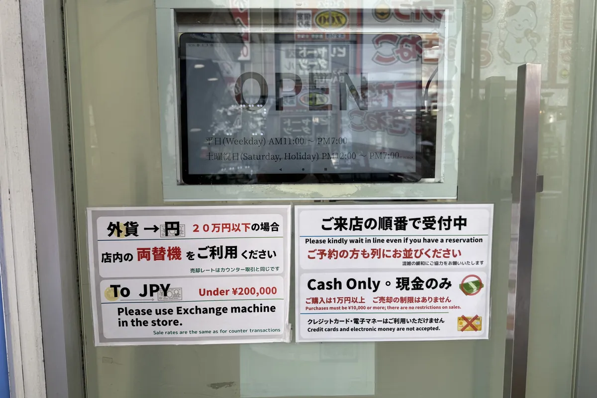 新宿西口の両替店ガラス扉に貼られた店舗ポリシー — 「Cash Only 現金のみ」「20万円以下は店内両替機をご利用」など重要情報がまとめて掲示